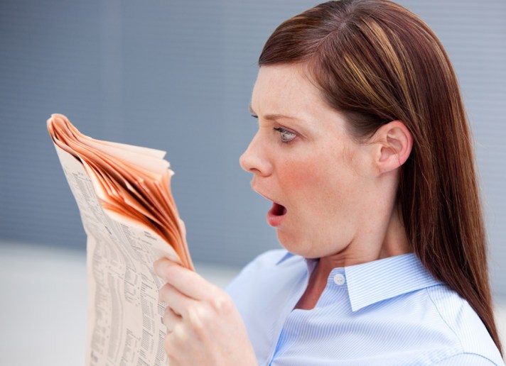 Astonished businesswoman reading newspaper