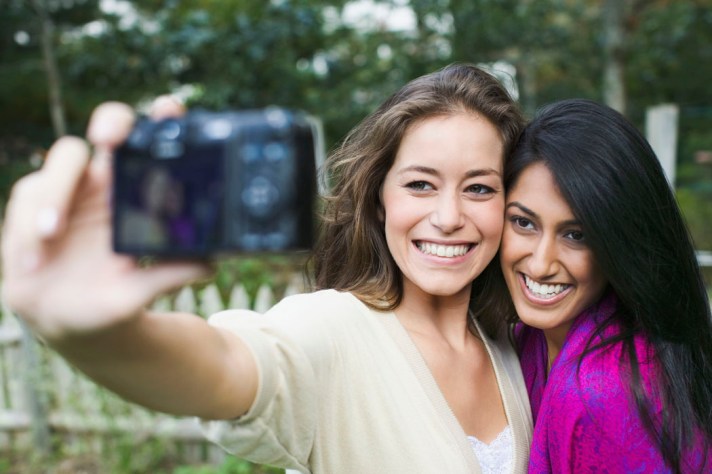 Two women taking picture of themselves with a digital camera