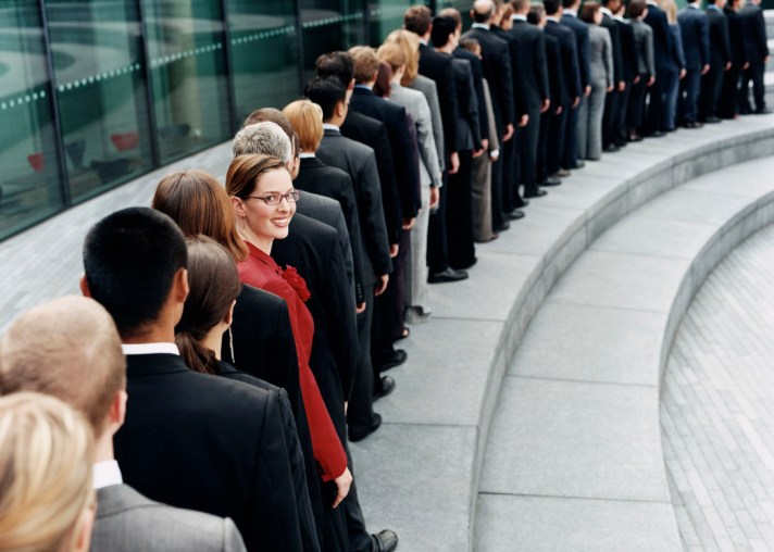 Businesswoman Standing Out in a Line of Business People Waiting Outdoors on a Step